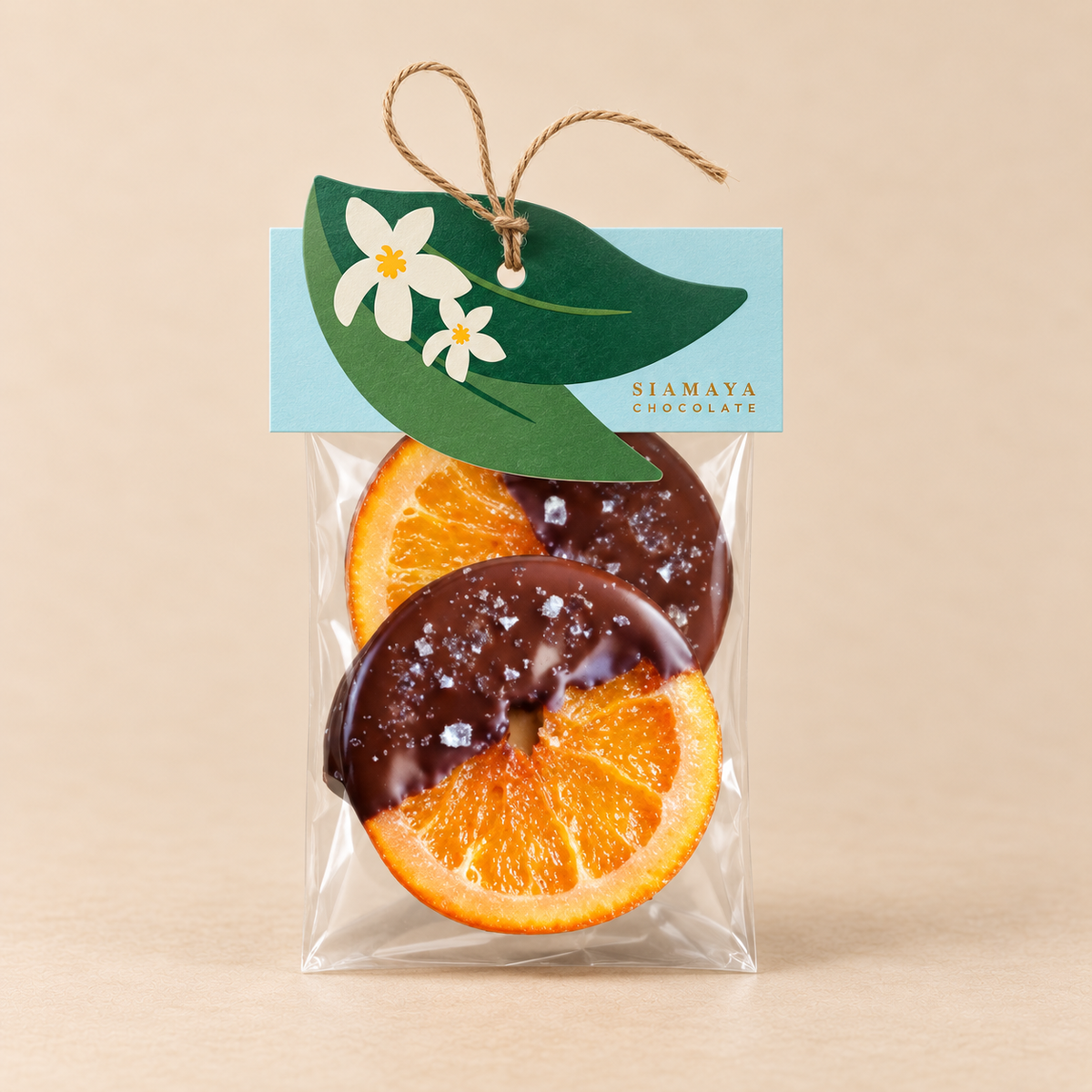 Siamaya Dark Chocolate Candied Orange, one 45 g clear bag with turquoise citrus-leaf header and twine, on a warm sand studio background.