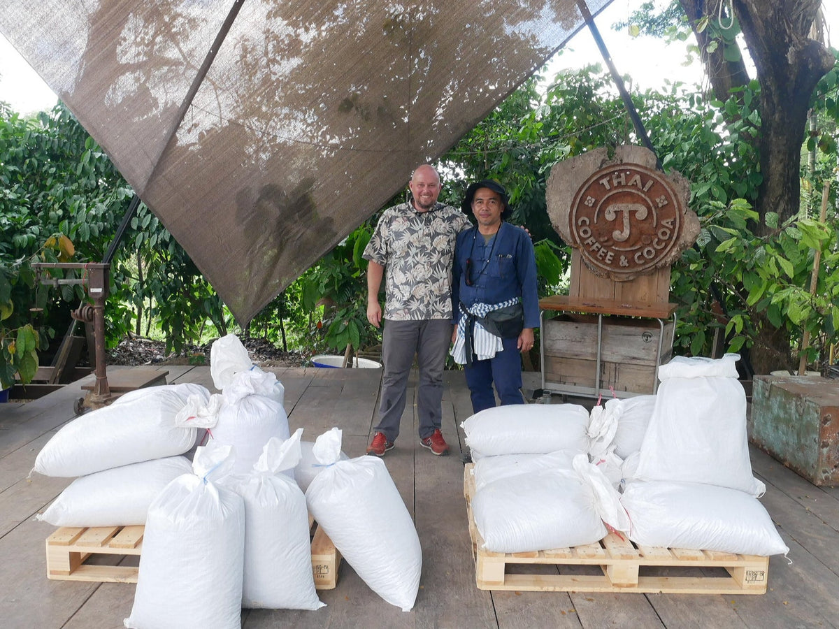 Neil and Pathom beside sacks of cacao at the supplier’s facility