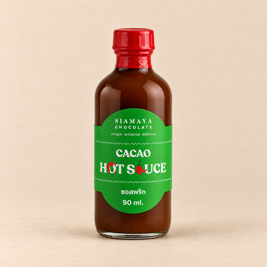 Siamaya Cacao Hot Sauce, 90 ml bottle with green label and red cap, on a warm sand studio background.