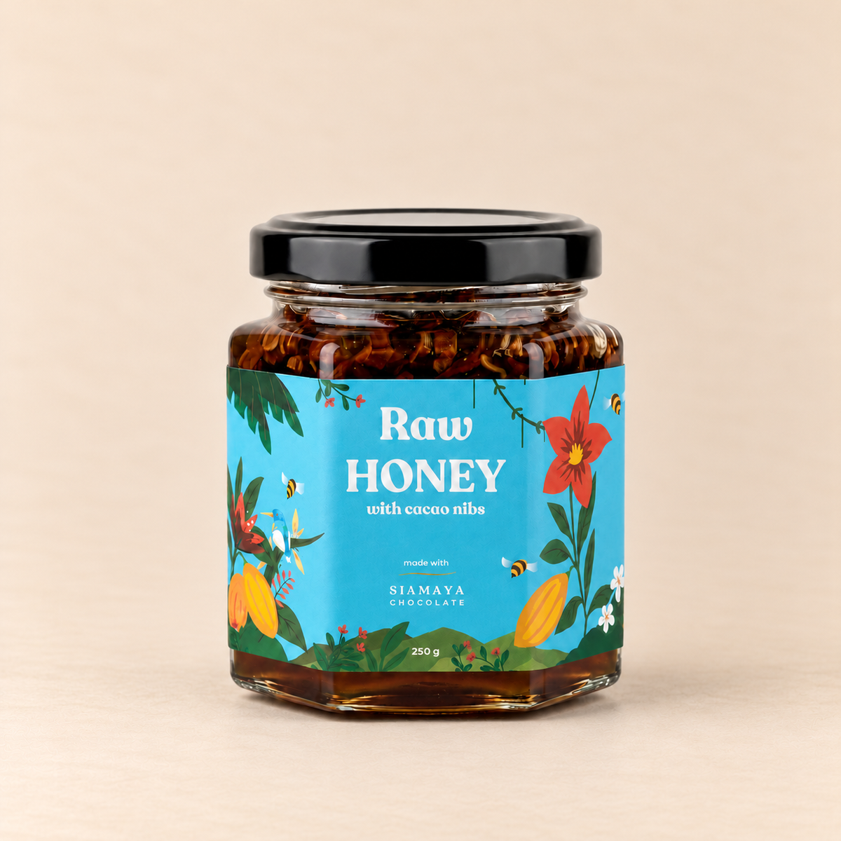 Siamaya Raw Honey with Cacao Nibs, 250 g jar with a black lid and turquoise floral label, on a warm sand studio background.